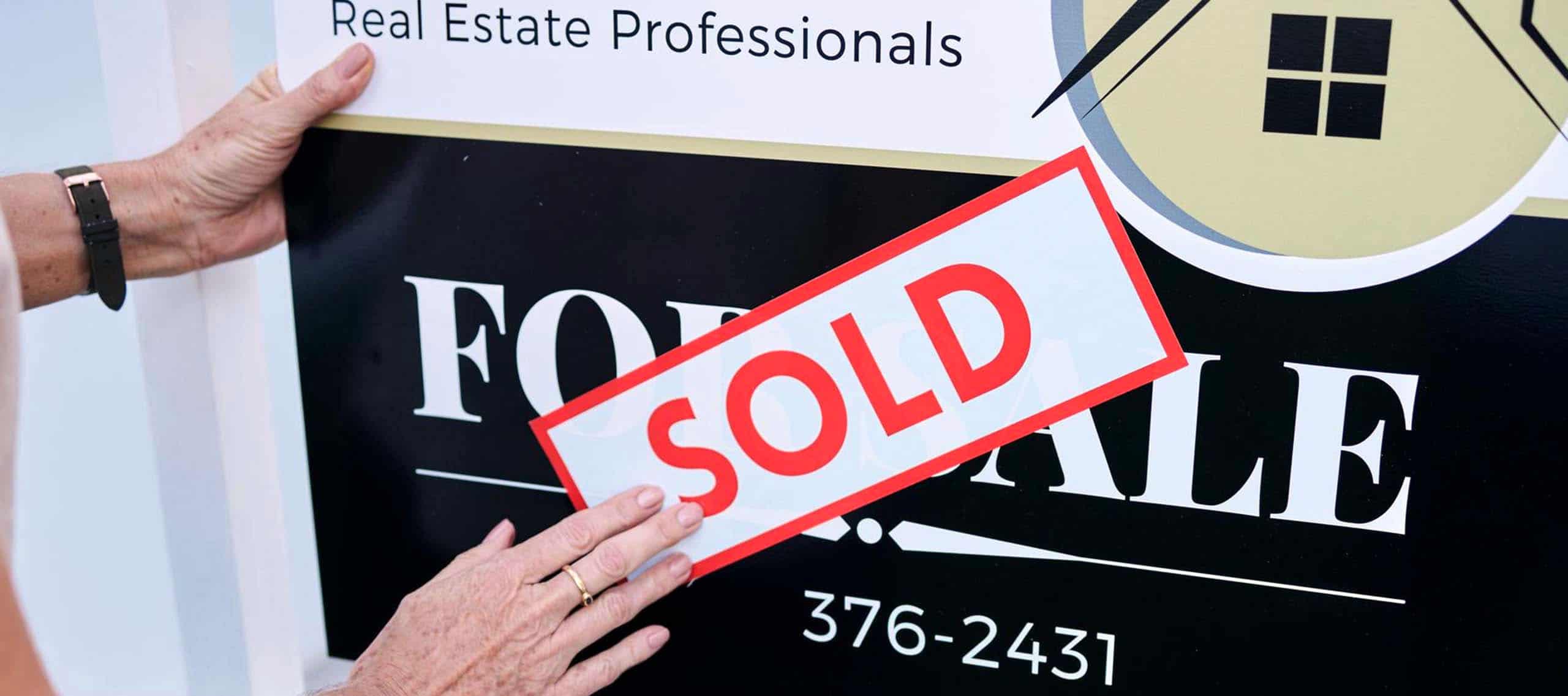 Real estate sold sign held by a person, indicating property sale success.